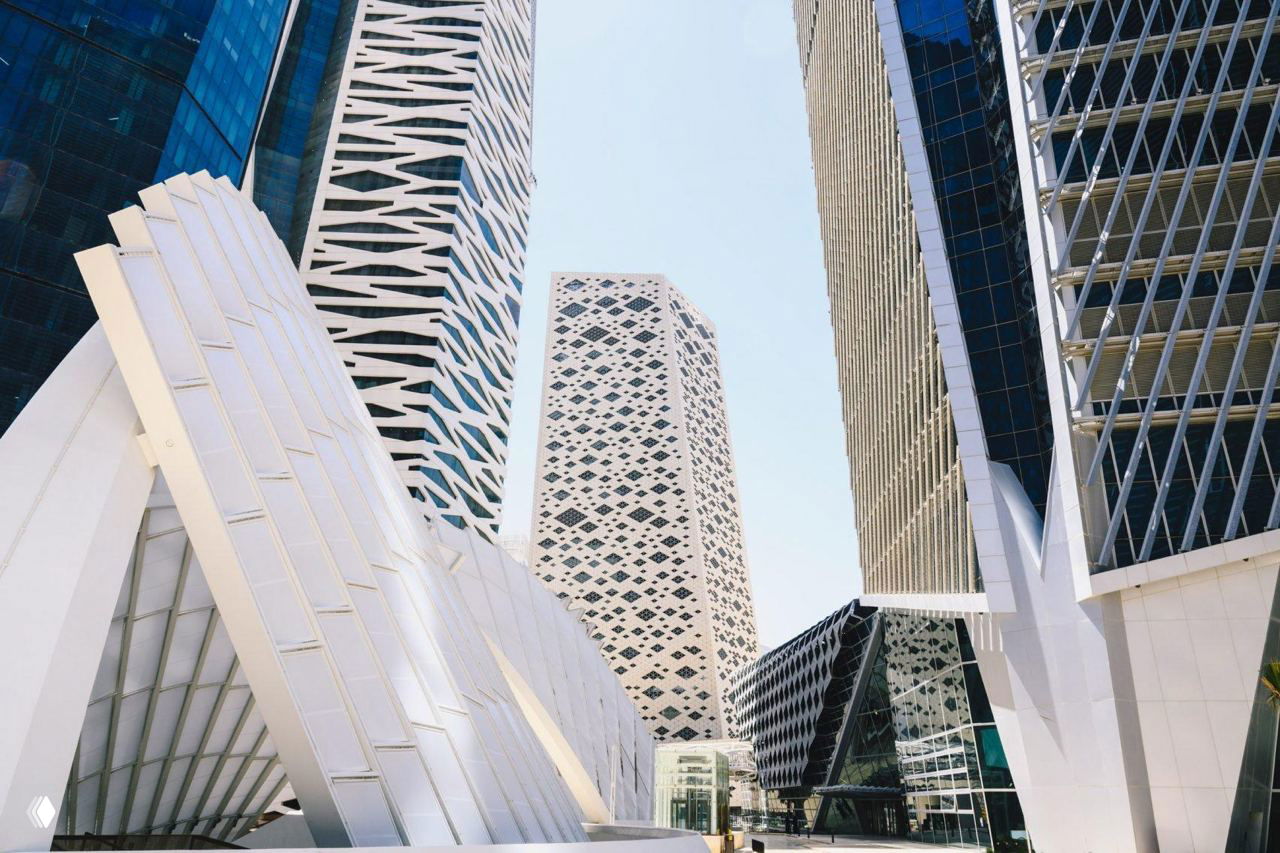 Современная архитектура в деловом районе Эр-Рияда: небоскрёбы с геометрическими фасадами на фоне светлого неба рядом с площадками для новой урбанистики.