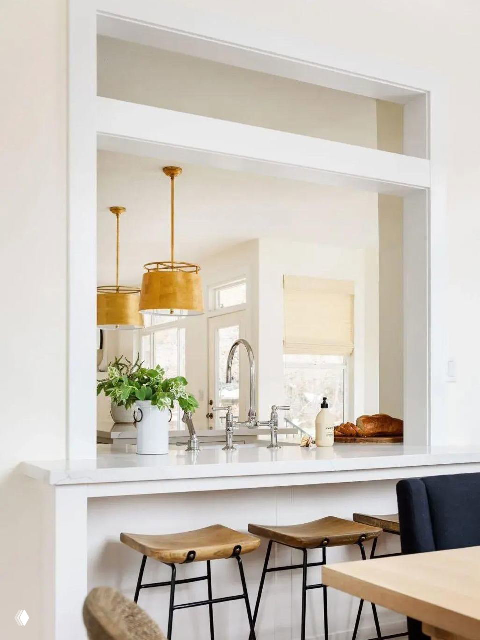Широкий прямоугольный проём‑окно между кухней и столовой, светлая столешница и три деревянных табурета у барной стойки