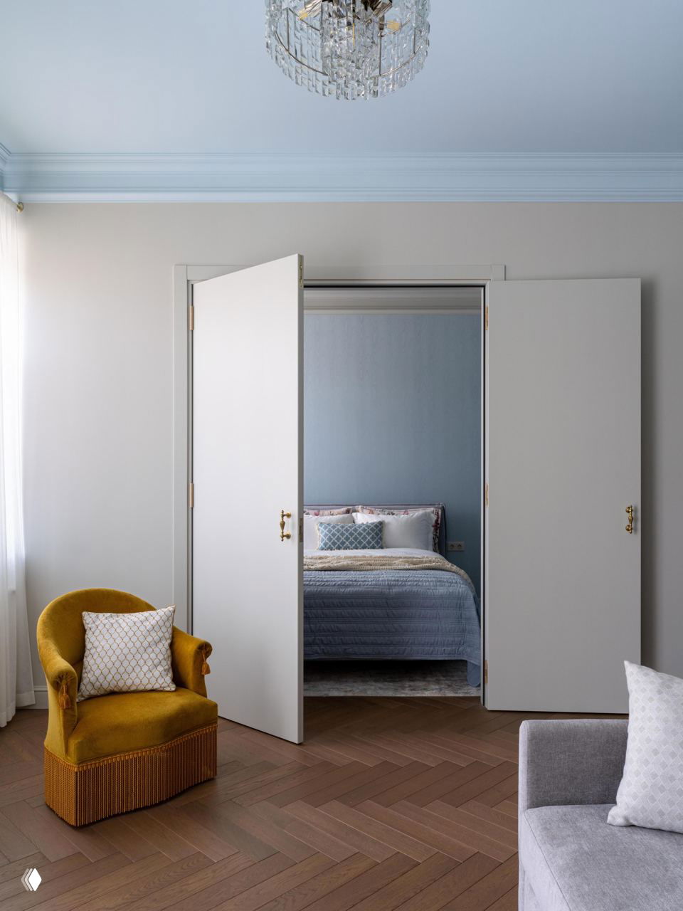 Раздвижные двери между гостиной и спальней, фрагмент жёлтого ретро-кресла и паркет ёлочкой, вид на выдержанную классическую планировку квартиры.