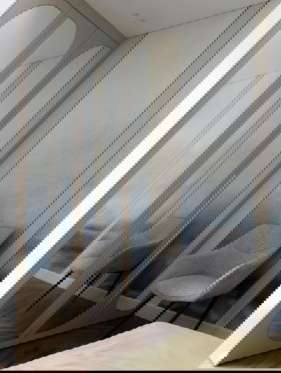 Спальня с зеркальным шкафом-купе и серым креслом, на фоне художественной стены с пастельными переходами в интерьере 42,5 м².