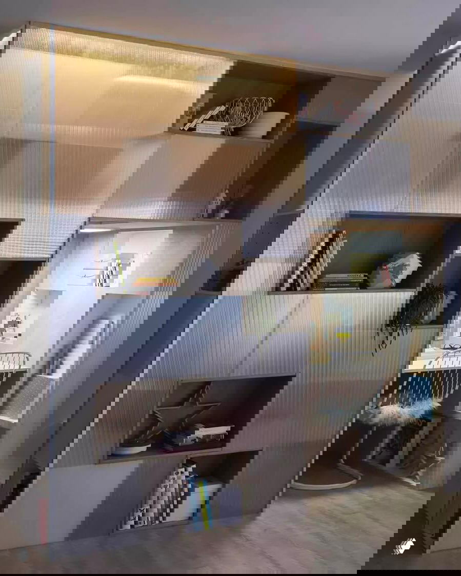 Рабочая ниша, отделённая полупрозрачными панелями и открытыми кубами для хранения: светлая зона с встроенным столом и полками для книг и декора.