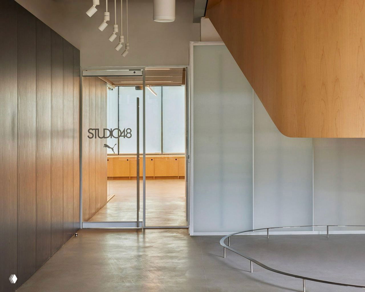 Входная зона Puma Studios: полупрозрачные стеклянные перегородки, деревянная облицовка и фрагмент винтовой деревянной лестницы, соединяющей уровни пространства.