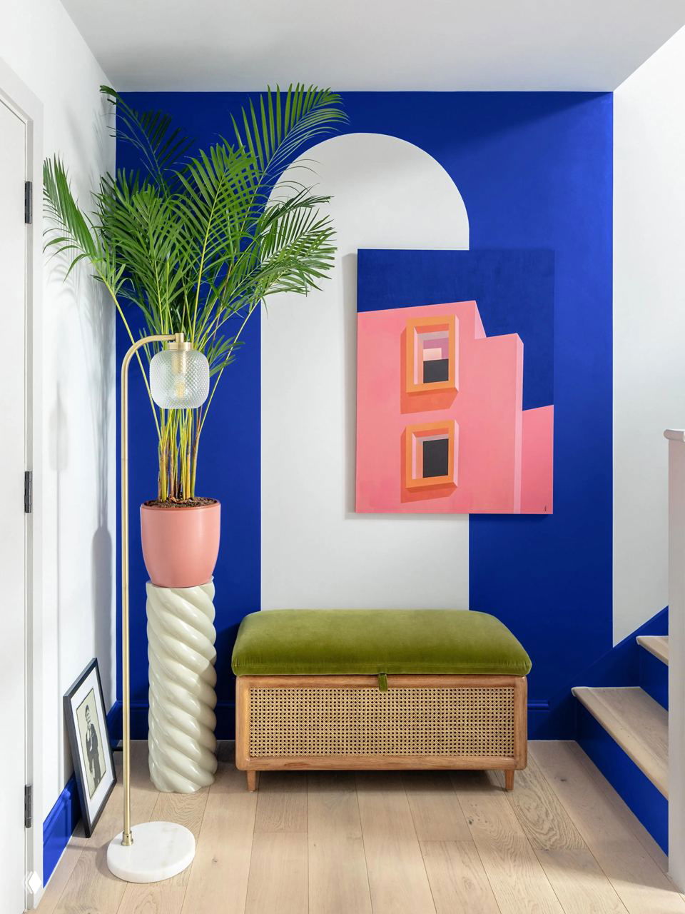 Яркая сине‑белая композиция с арочным мотивом, большая пальма в розовом горшке и плетёная скамья с зелёной бархатной обивкой на светлом полу.
