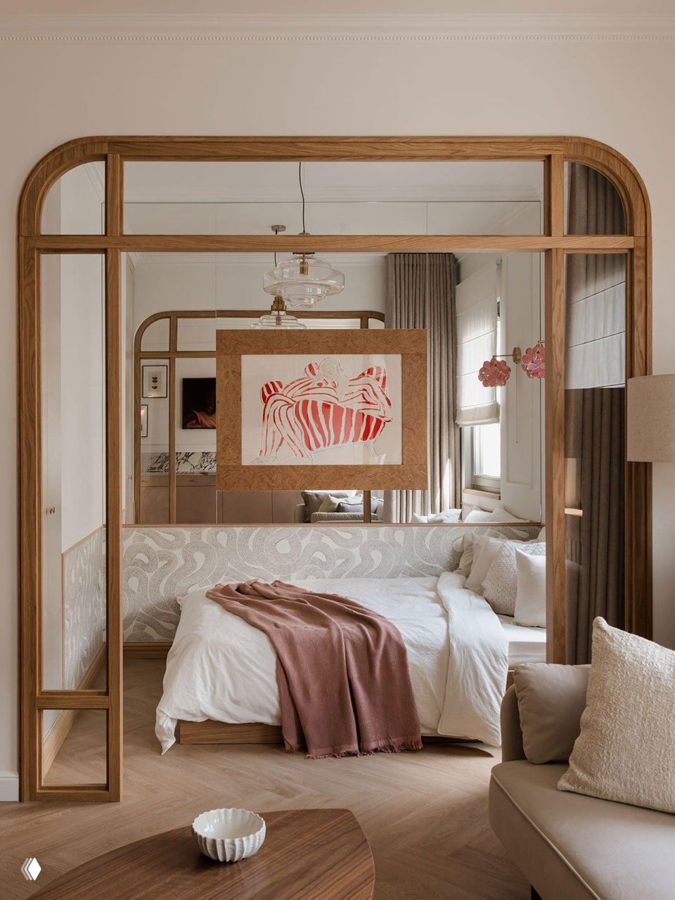 Вид на спальню через деревянную стеклянную перегородку: кровать с текстилем в мягких тонах, зеркало и декоративная картина над изголовьем.