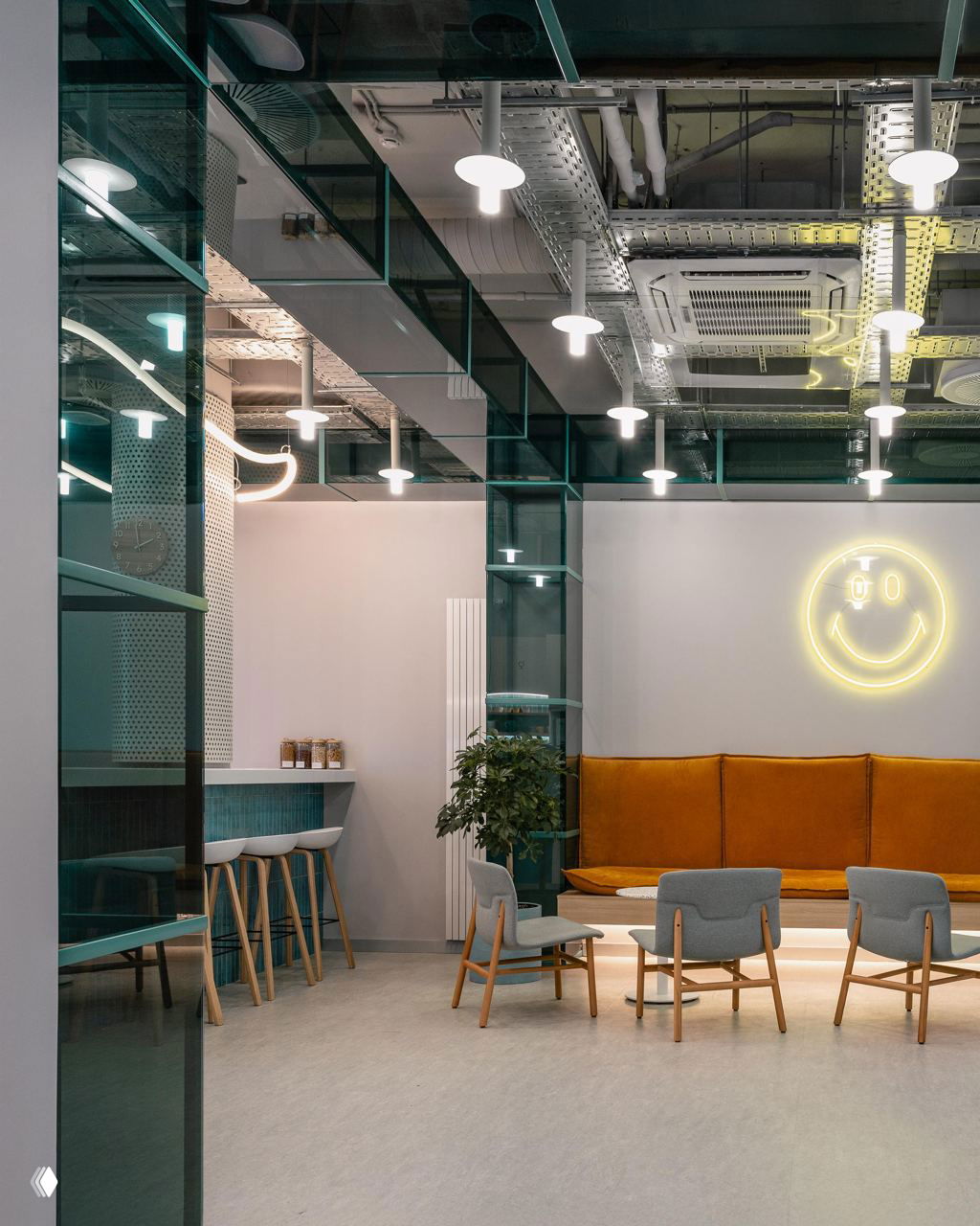Панорамный вид через зелёные стеклянные перегородки на зону с оранжевым диваном, высокими потолками и неоновой вывеской в форме улыбки.