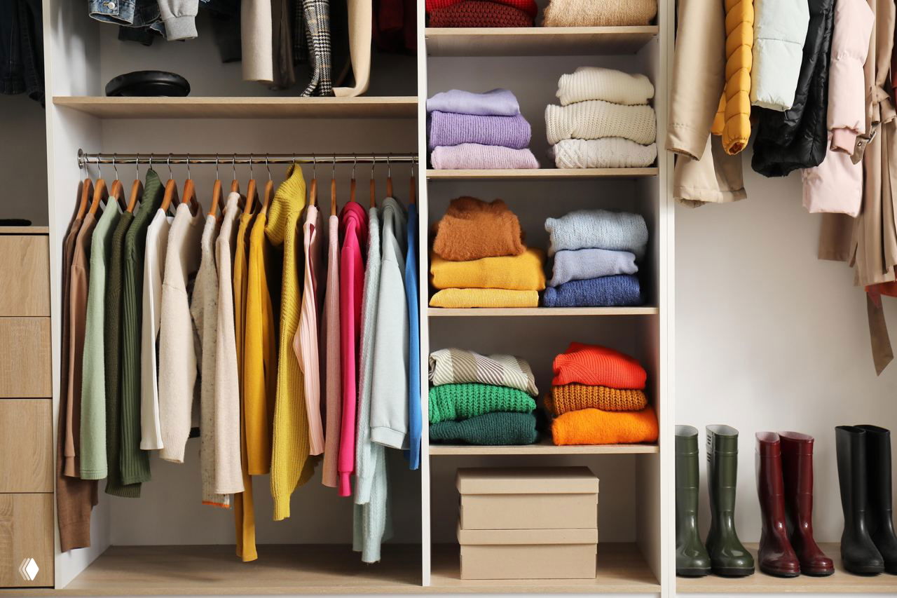 Открытый шкаф с аккуратно развешанной одеждой и сложенными свитерами разных цветов — пример упорядоченного гардероба после расхламления.