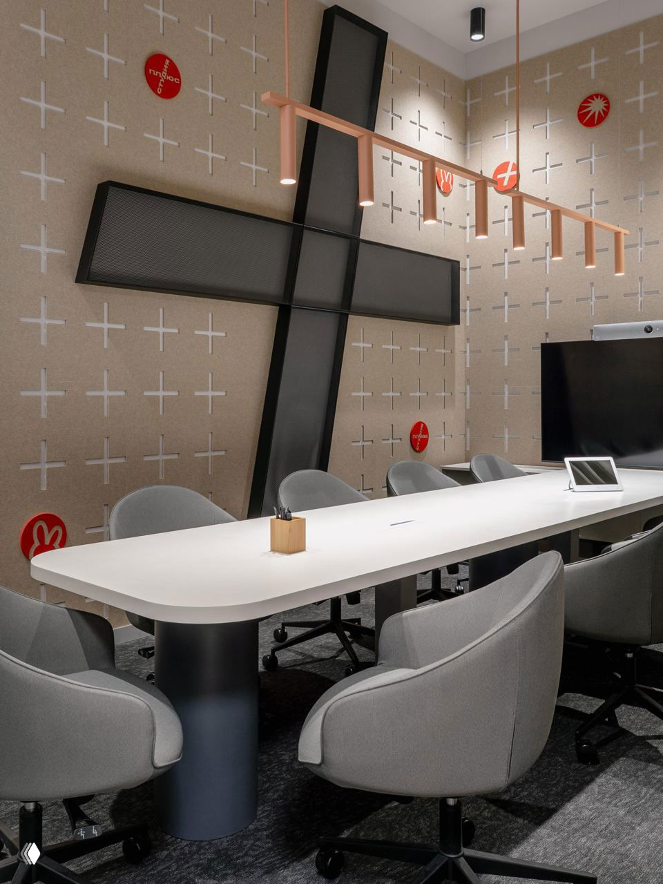 Современный переговорный стол, крупная декоративная крест-структура на стене и минималистичные серые кресла вокруг длинного белого стола.