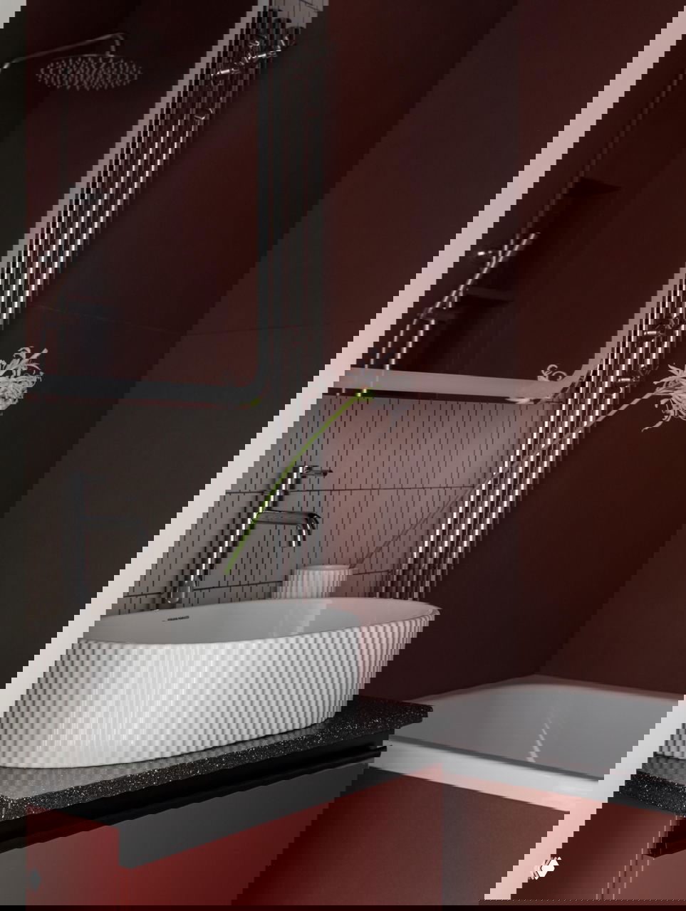 Ванная комната в проекте: рифлёная белая раковина на тёмной столешнице, бордовые стены, хромированная арматура, ванна и декоративный цветок.