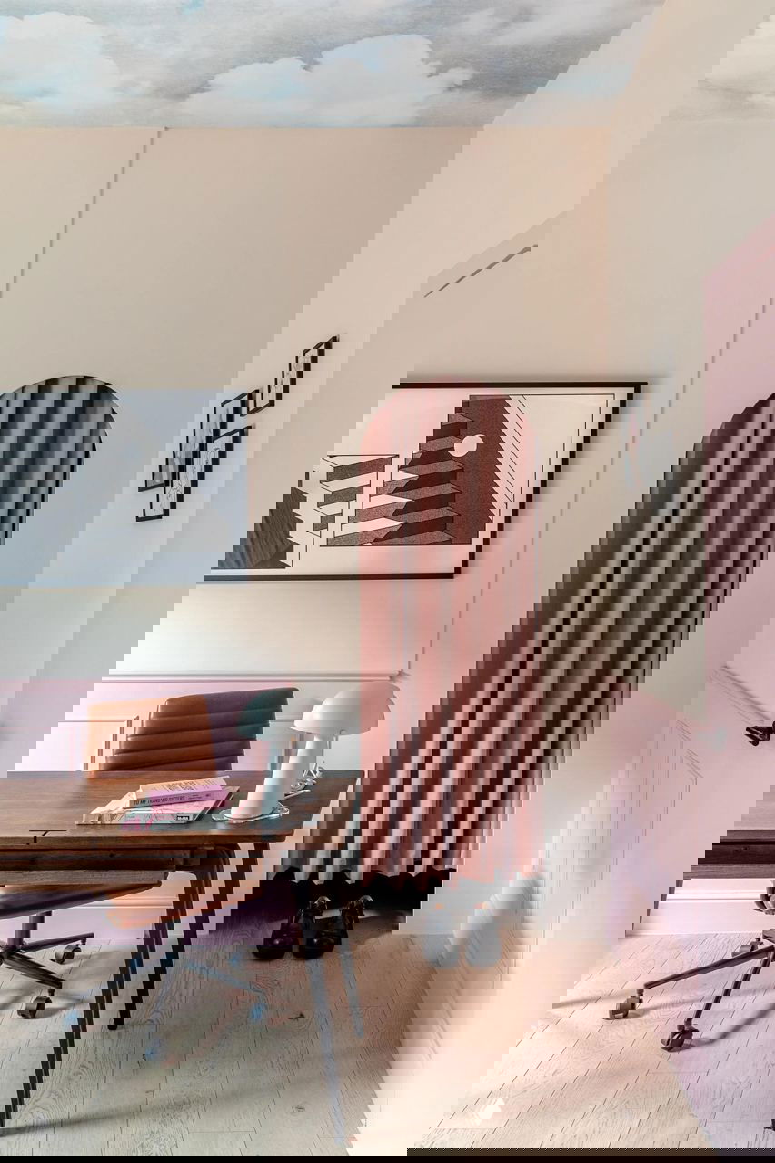 Рабочая зона с розовыми стенами и арочным проёмом, за которым скрыта шторка; в кадре деревянный стол, кресло на колёсах и классические декоративные элементы.