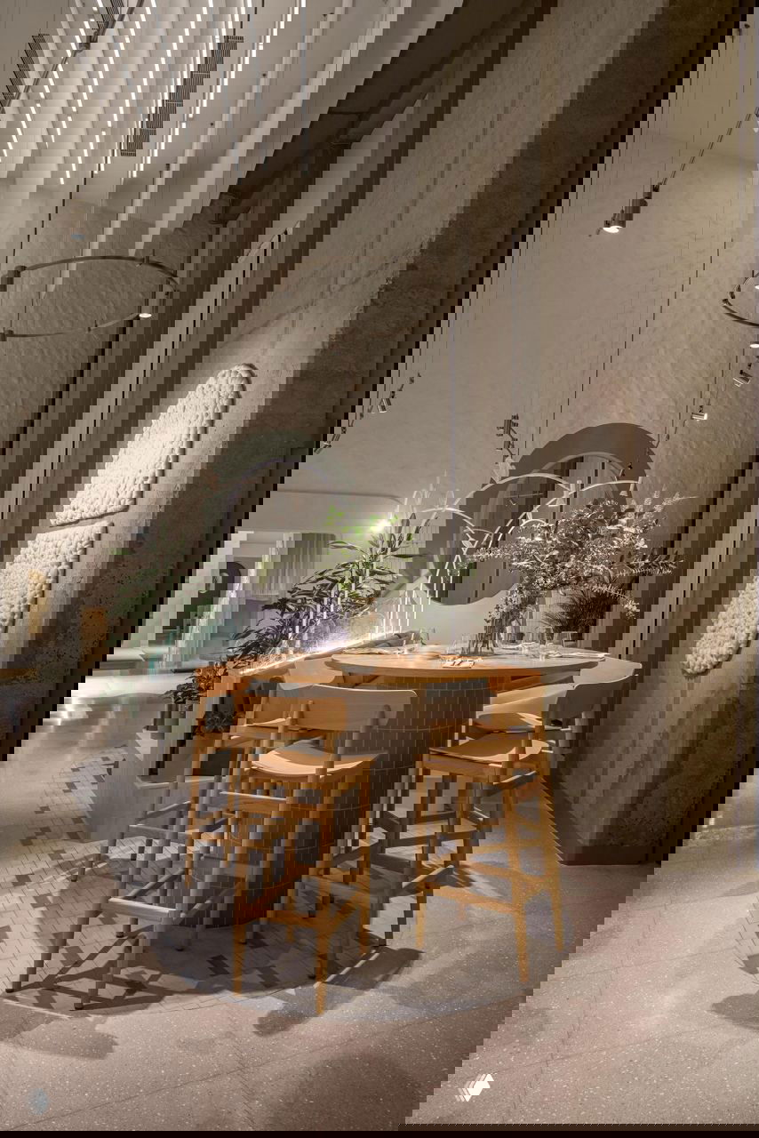 Барная зона с высоким круглым столом и деревянными барными стульями; комбинирование плитки, бетона и зелёных растений создаёт уютную островную композицию.