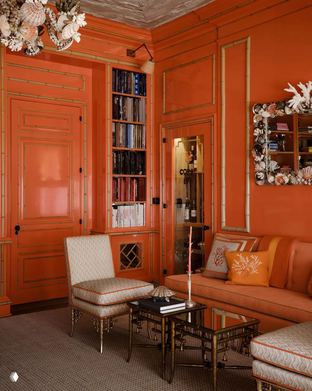 Гостиная зона с лакированными коралловыми панелями, золотыми бамбуковыми молдингами, диваном и карнизами в единой тёплой палитре интерьера.