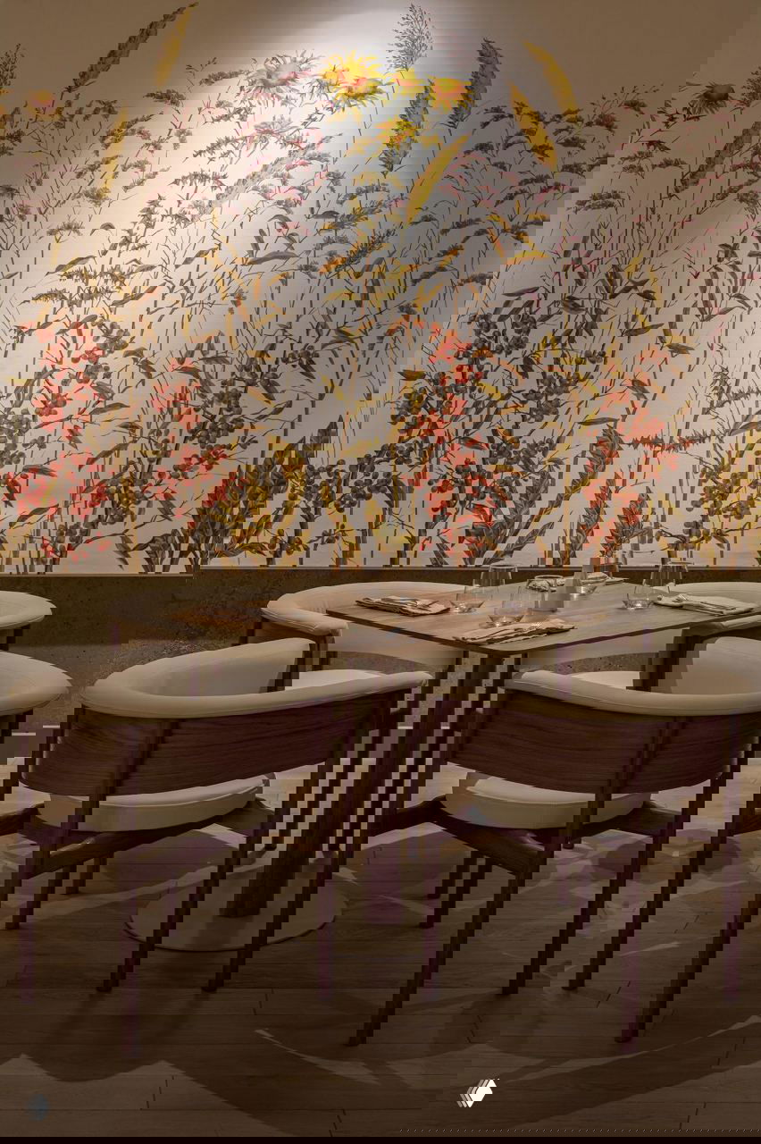 Обеденная зона с настенной росписью полевых цветов, деревянный стол и мягкие кресла — тёплая гамма и детализированный растительный рисунок на стене.