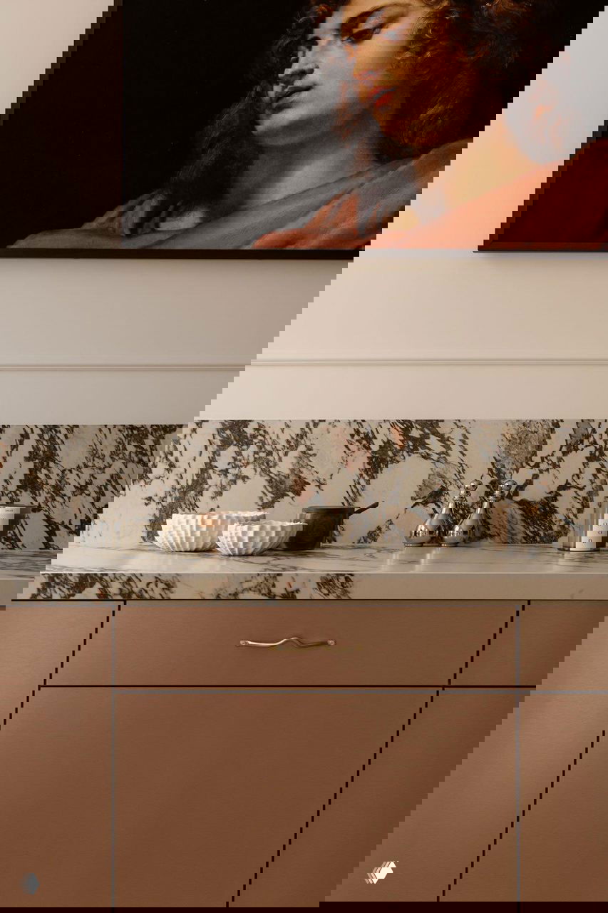 Деталь кухонной столешницы: контрастный мрамор с выраженными прожилками, матовые фасады шкафов и аккуратные декоративные предметы на рабочей поверхности.