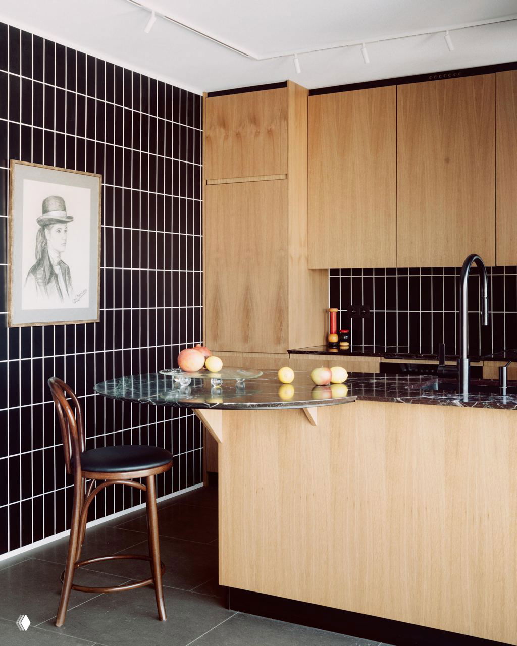 Кухонная зона с тёмной вертикальной плиткой и деревянными фасадами; изящная круглая мраморная столешница-барная стойка с расставленными фруктами для атмосферы.