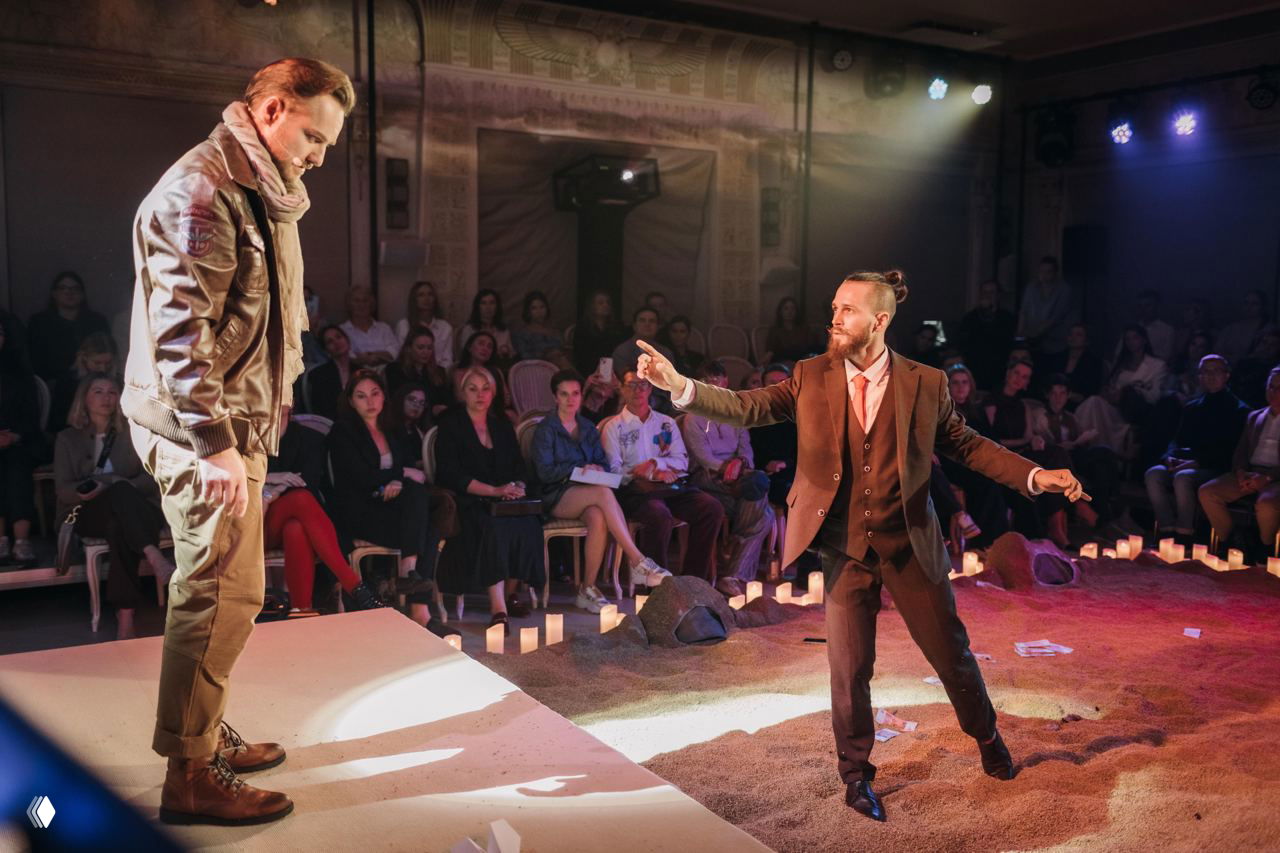 Камерная театральная сцена: двое актёров на помосте, публика вблизи, свечи создают тёплую интимную атмосферу.