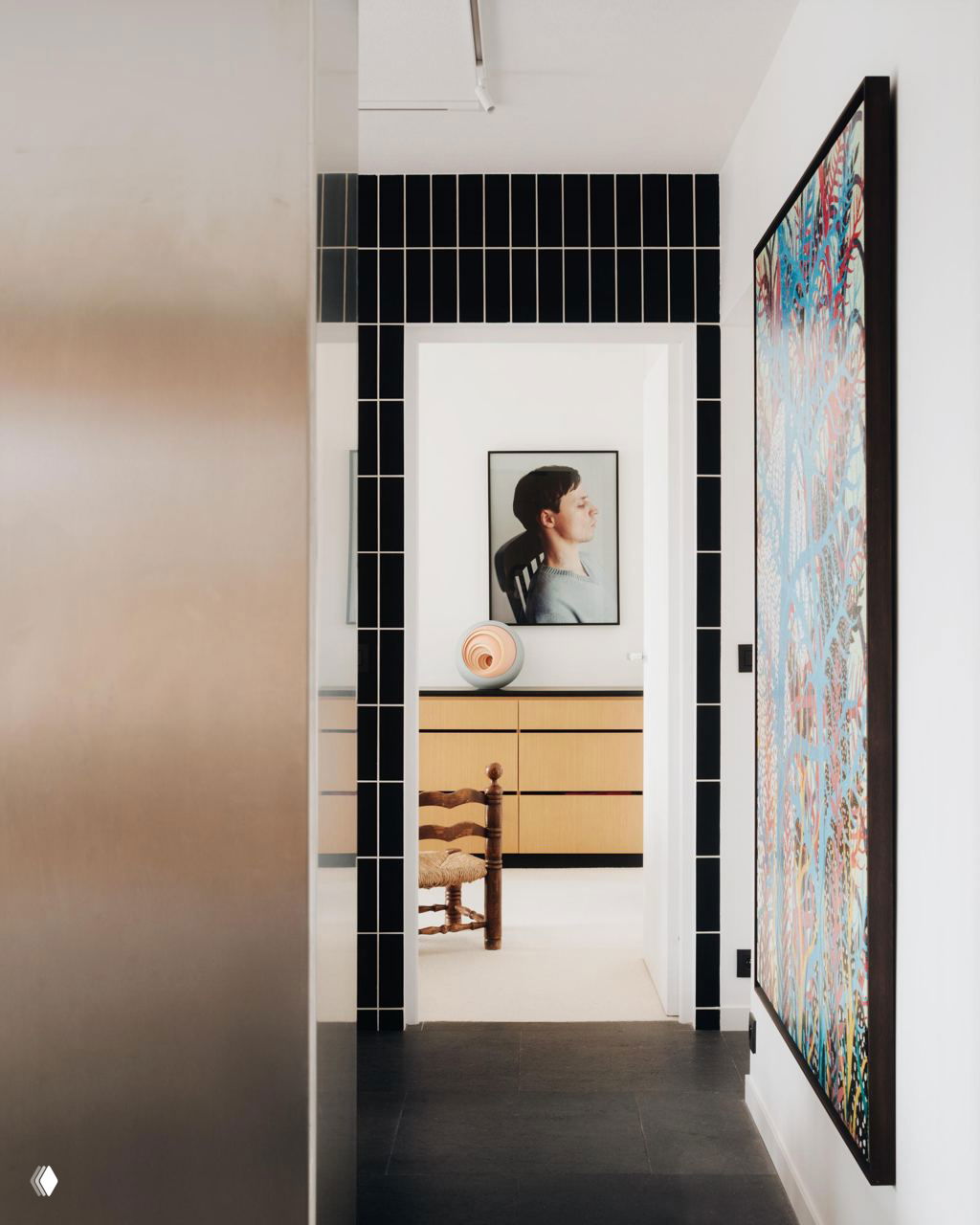 Вид через дверной проём: композиция из картин, комод светлого дерева и спокойный минималистичный интерьер, акценты на искусстве и мебели.