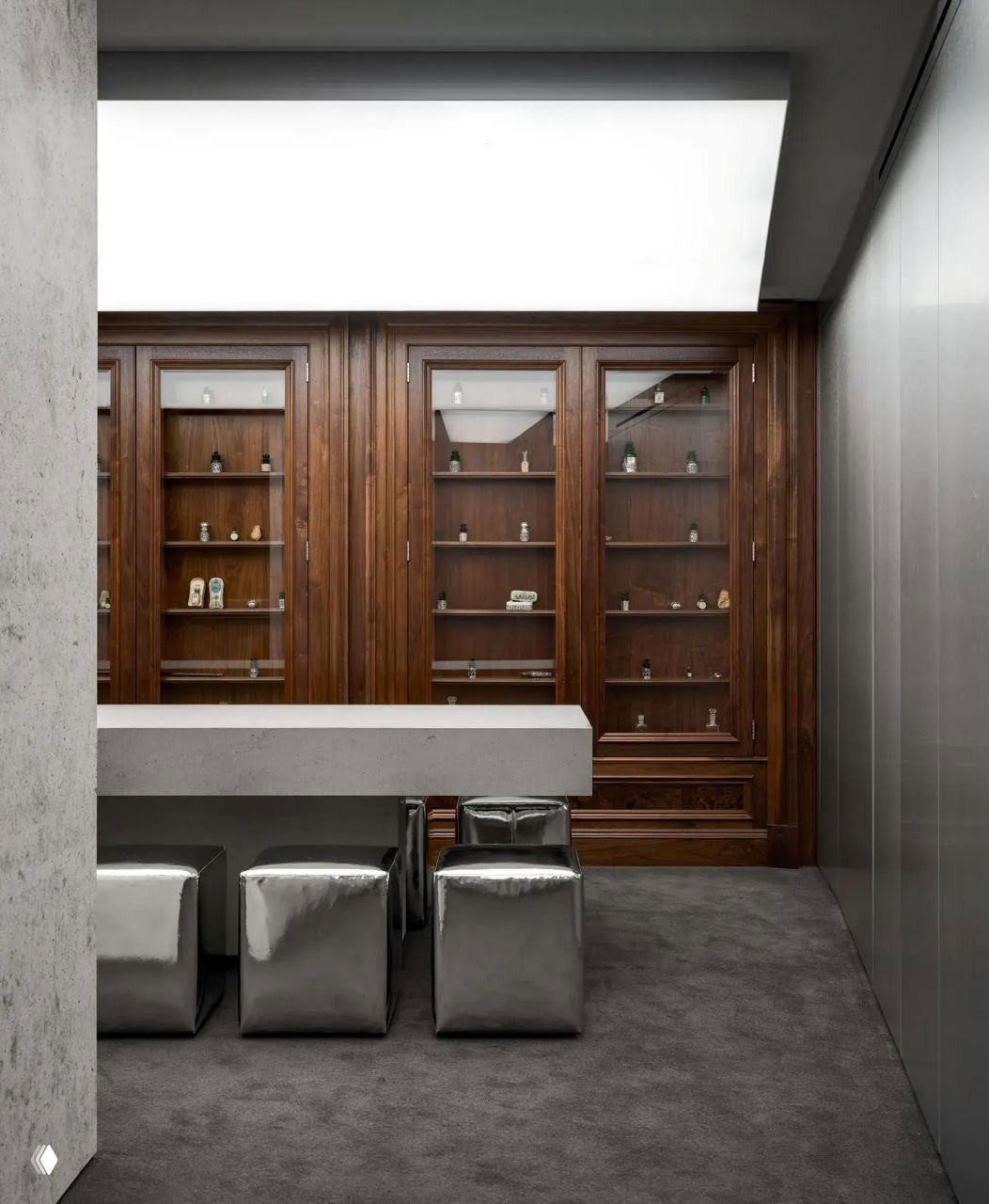 Узкая зона с барной стойкой и металлическими кубическими пуфами на фоне витрин с коллекцией флаконов — эстетика регентства в современной интерпретации