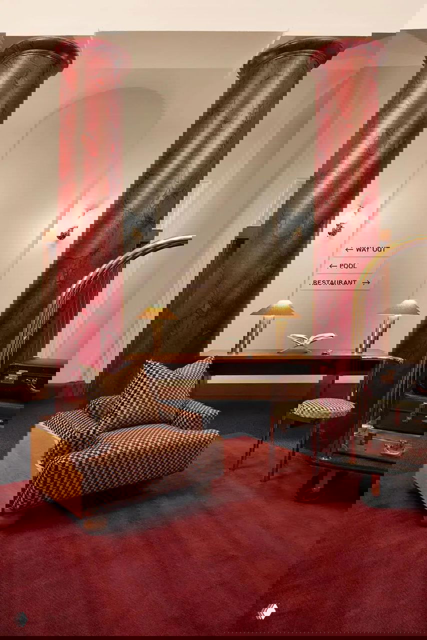 Интерьерная сцена с креслом в мелкий геометрический принт, красными колоннами и дорожными указателями — сочетание тканей Kirkby и архитектурного контекста.