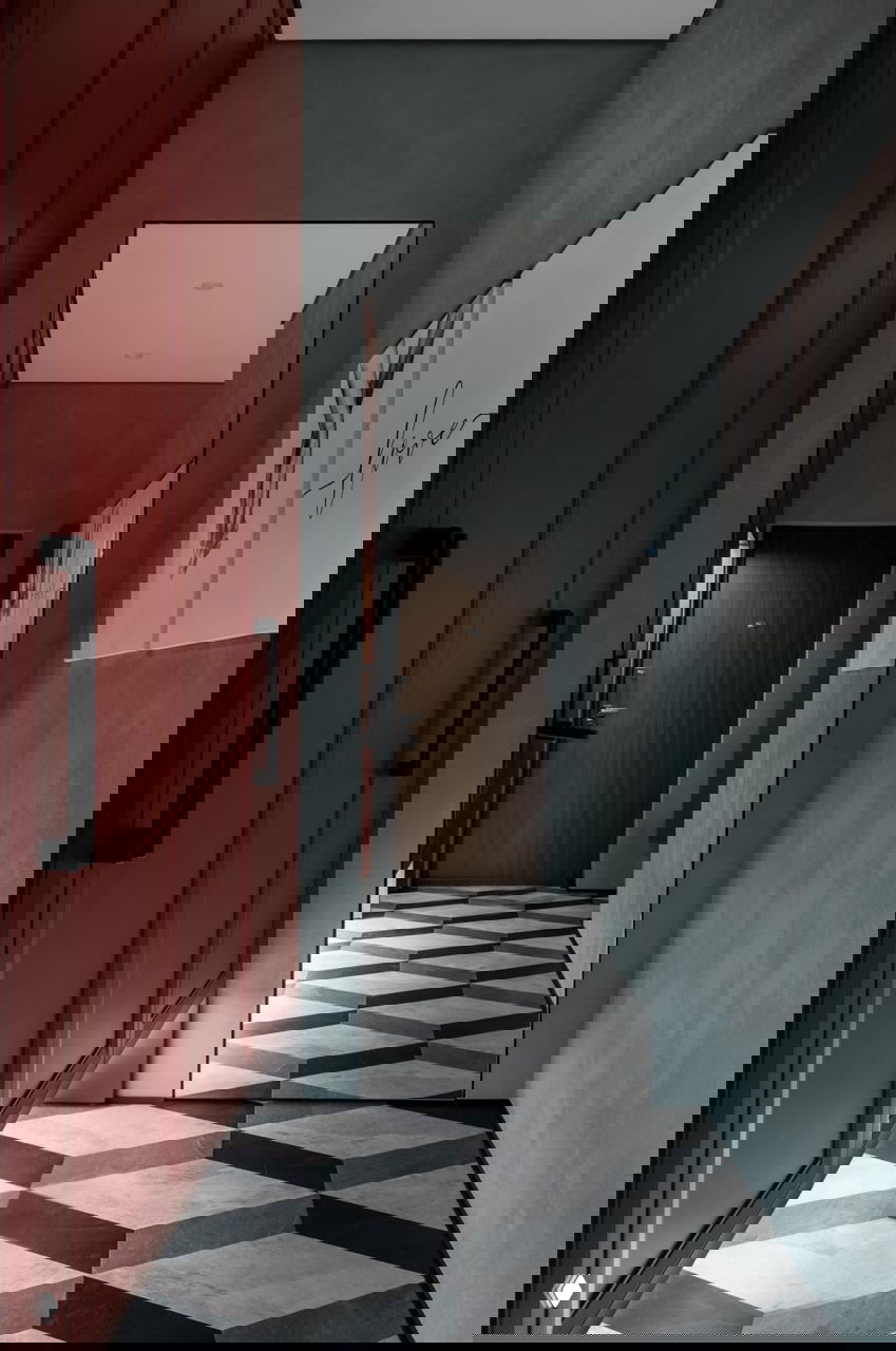 Прихожая с высоким зеркалом, ярко‑красным встроенным шкафом и контрастной геометрической плиткой на полу — сочетание цвета и материалов в холле квартиры.