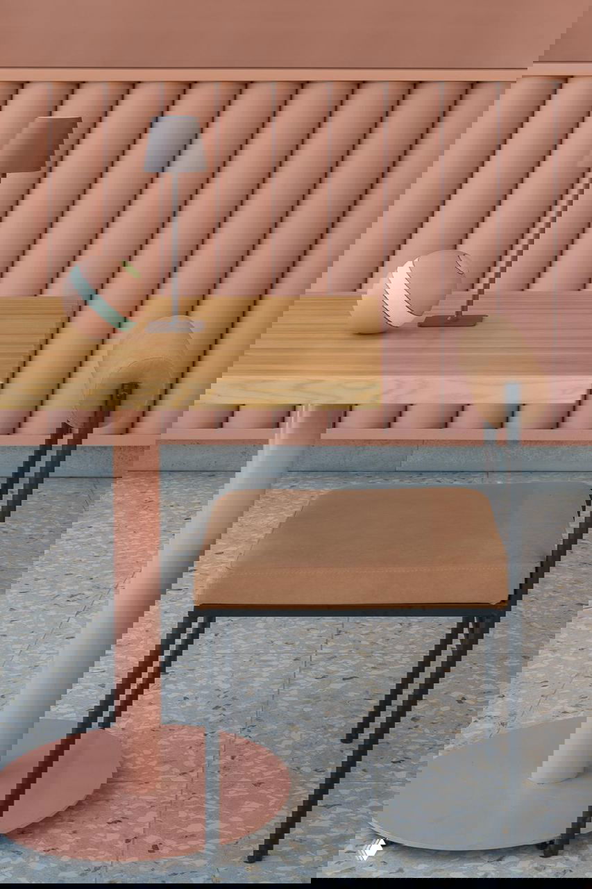 Стол и стул в коралловых и натуральных древесных тонах на фоне ребристой барной панели; на столе декоративный мяч и настольная лампа, минималистичная мебель.