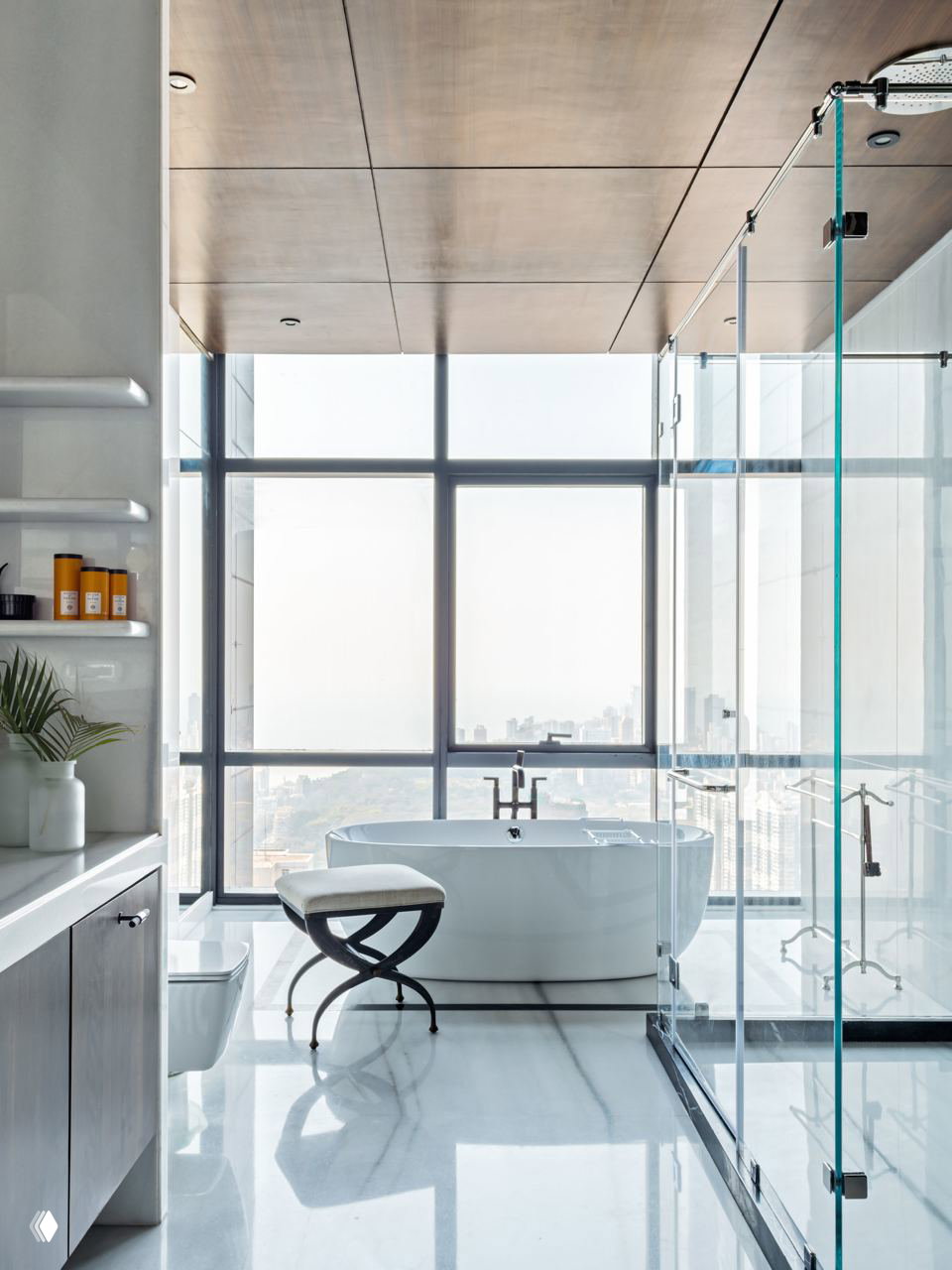 Ванная с панорамным окном: белая отдельностоящая ванна и стеклянная душевая кабина на фоне городского пейзажа, высокий потолок и светлая мраморная отделка.