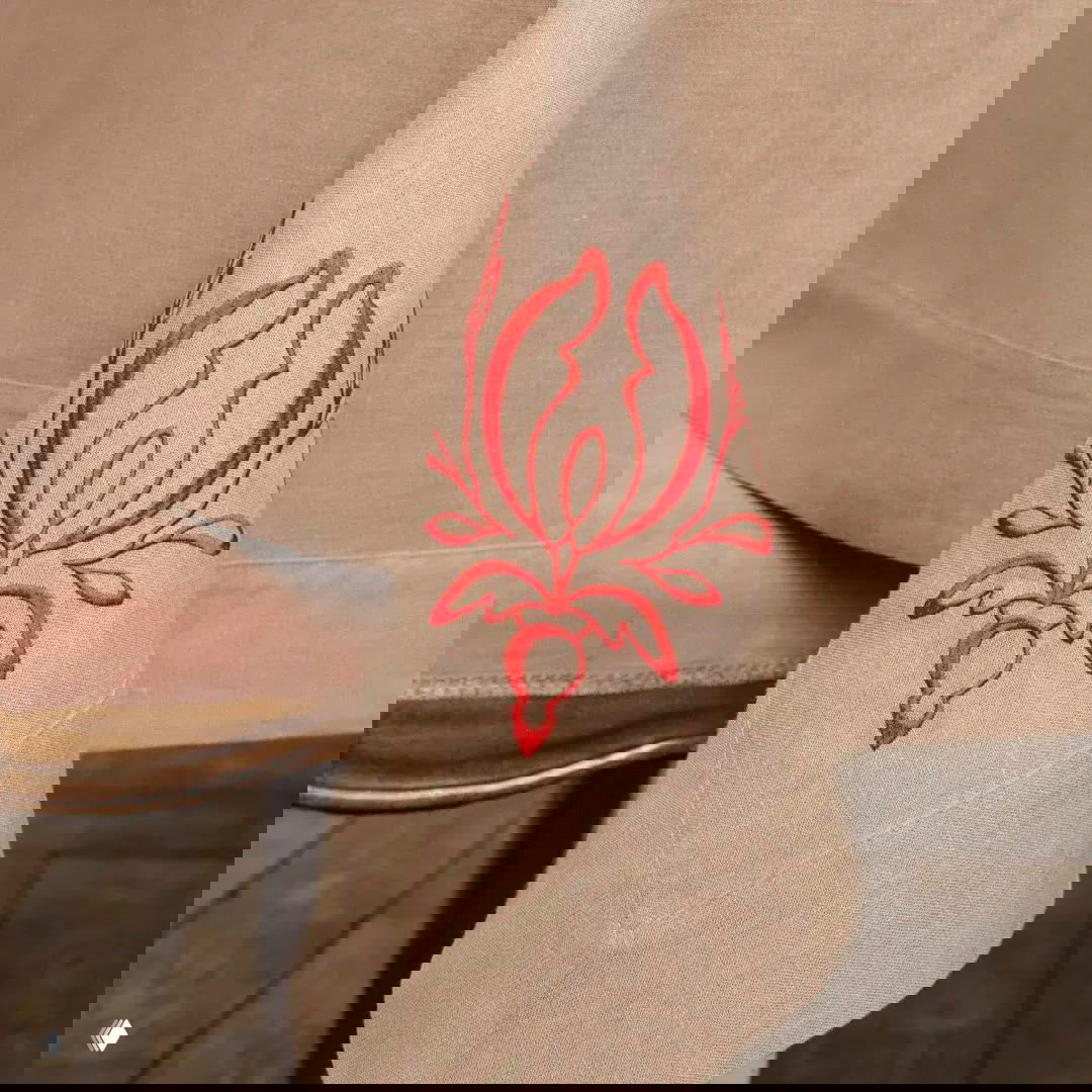 Угол скатерти с декоративным алым мотивом якобинского цветка: крупный план вышивки на натуральном льне.