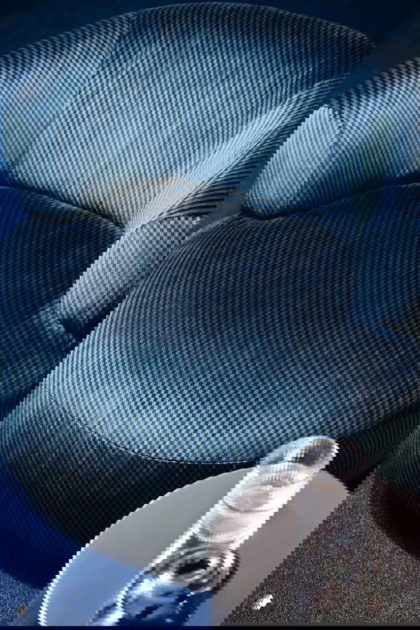 Крупный план округлого кресла в узкую синюю полоску на синем ковре, демонстрирующий текстуру и направление ворса ткани Kirkby в интерьерной композиции.
