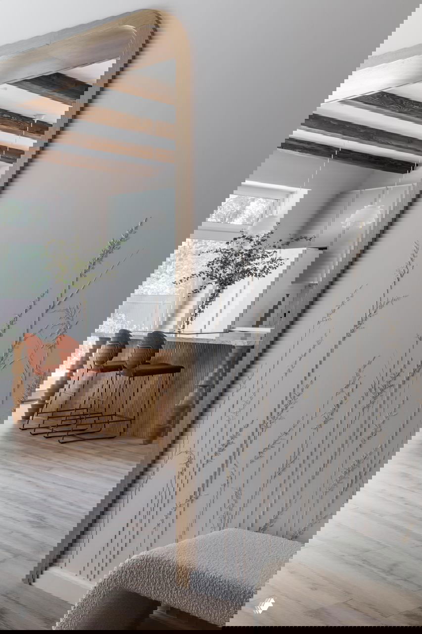 Проём со скруглёнными краями, через который видна кухня-барная зона; большое зеркало в деревянной раме и декоративная отделка стены растительным орнаментом.