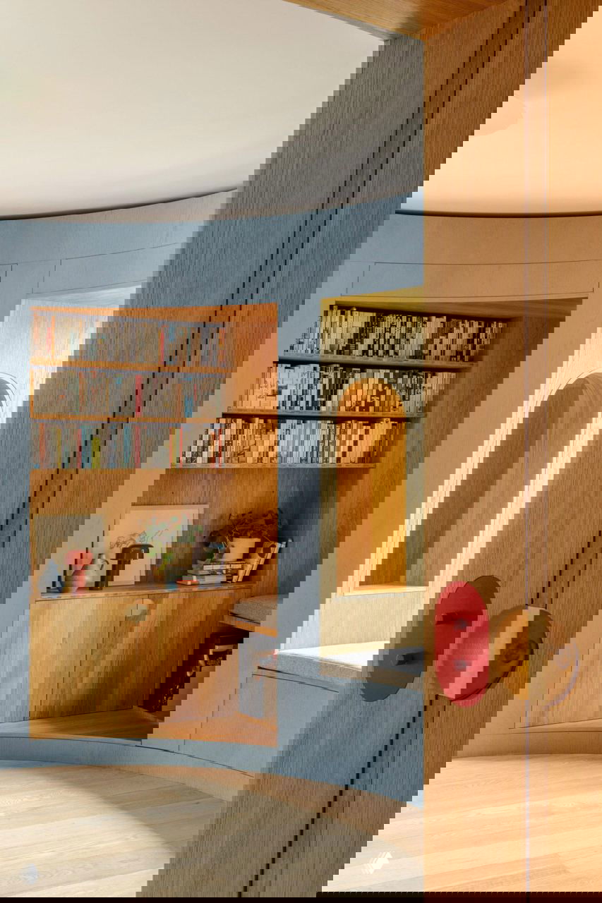 Крупный план внутренней части круглой библиотеки: синие внешние панели, открытые полки из дуба и встроенные ниши для чтения.