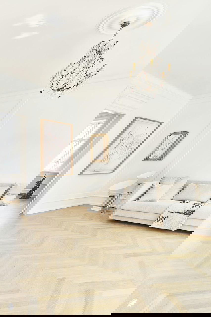 Светлая гостиная в реставрированном доме: хрустальная люстра, белые стены, мягкий диван и аккуратный паркет — интерьер Аннет Кьерульф.