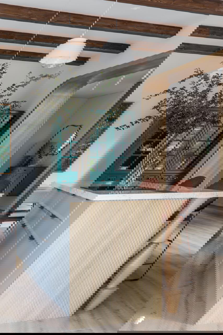 Кухонный остров с мраморной столешницей и вертикальной деревянной фактурой, барные стулья терракотового цвета и ваза с зелёной композицией на столешнице.