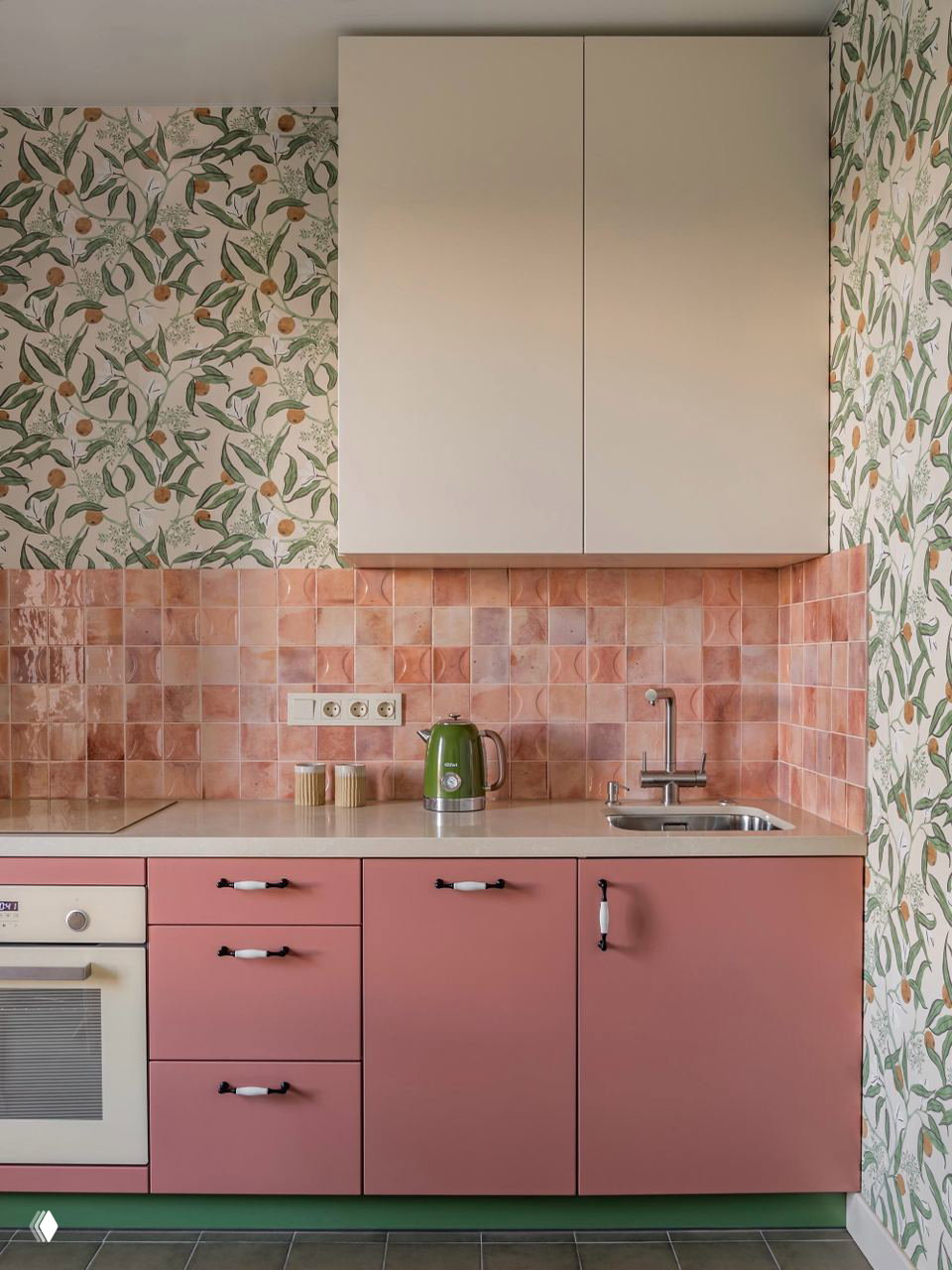 Кухонный фрагмент с матовыми пудрово-розовыми фасадами, розовой глазурованной плиткой фартука, зелёный чайник и декоративные растительные обои на стене