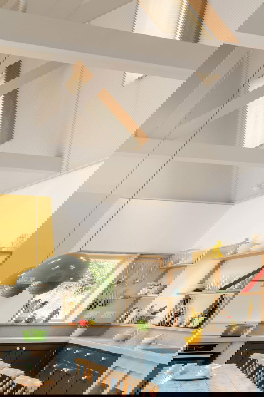 Светлая кухня с высокими скатными потолками, белыми балками и тёмно-синими нижними шкафами на фоне деревянных вставок.