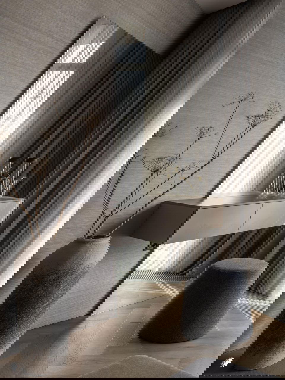 Косметический уголок у окна: плавающая консоль, высокий грубый вазон с сухими ветками и мягкий пуф на фоне струящихся штор в проекте Жанны Бондаренко.