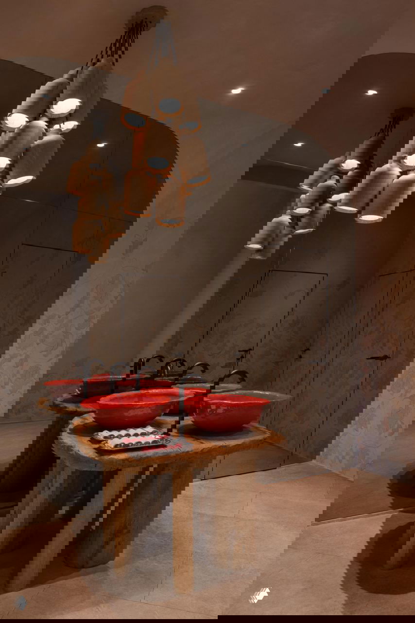 Туалетная зона и умывальники: круглые красные керамические раковины, массивные деревянные столы, зеркало и приглушённое светление из подвесных ламп.