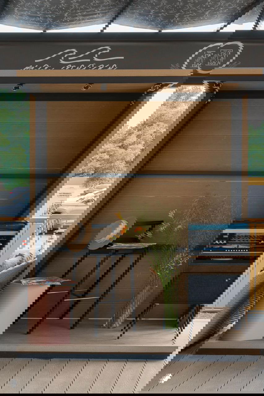 Небольшая сценическая зона на террасе с барным табуретом, шляпой и виниловым проигрывателем рядом с вазой с цветами — атмосферная деталь пляжного ресторана.