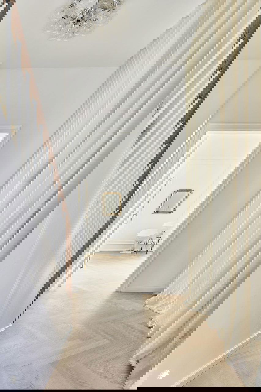 Лестничный холл с нейтральными шторами, светлым паркетом и декоративной хрустальной люстрой в глубине — интерьер реставрированного дома.