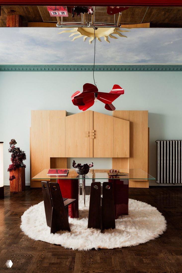 Стол и обеденная зона: стеклянная столешница, низкие красные опоры и тёмные деревянные стулья на круглом пушистом ковре в интерьере Познани.