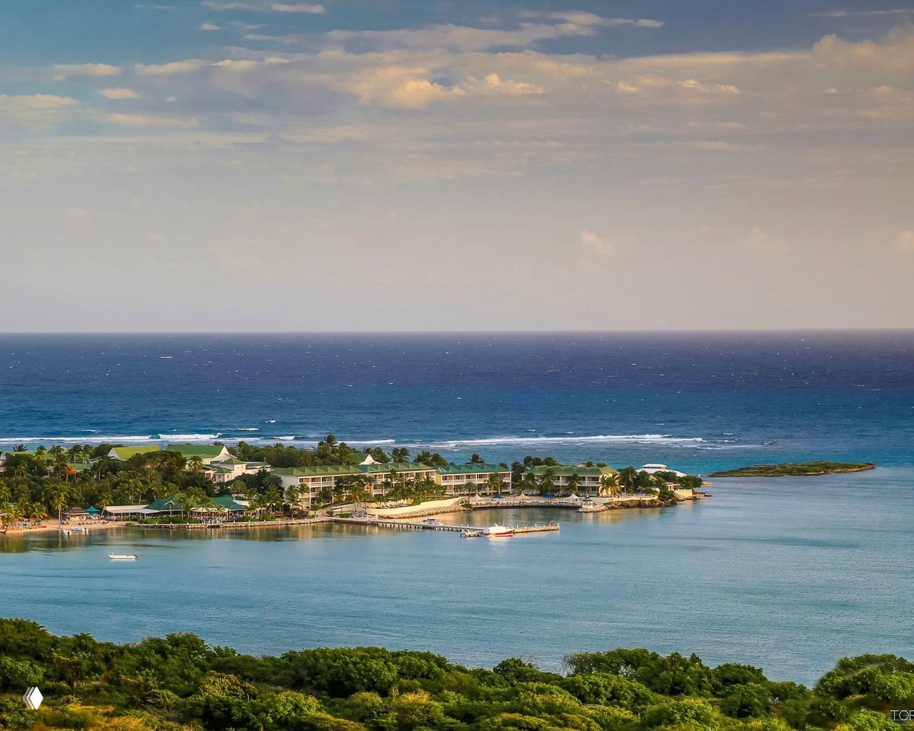 Тропический побережный участок с зелёной растительностью, прибрежными отелями и прозрачной бирюзовой водой в спокойную погоду у берега.