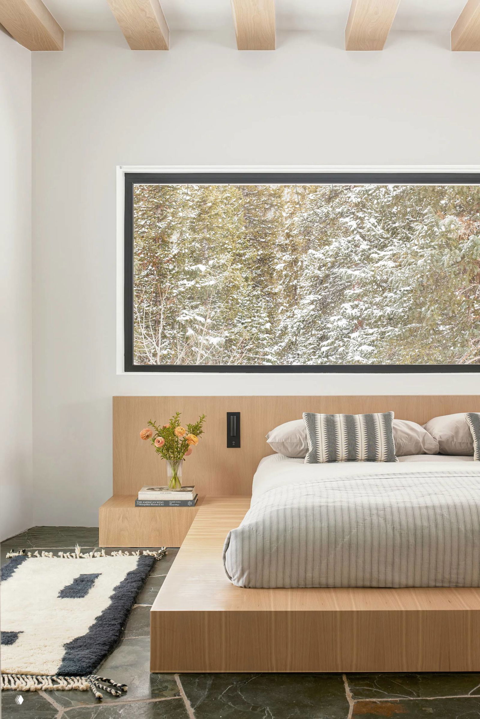 Спальня в шале: платформа-кровать и прикроватная ниша из светлого дуба, большое горизонтальное окно с видом на зимний лес и строгий минималистичный текстиль.