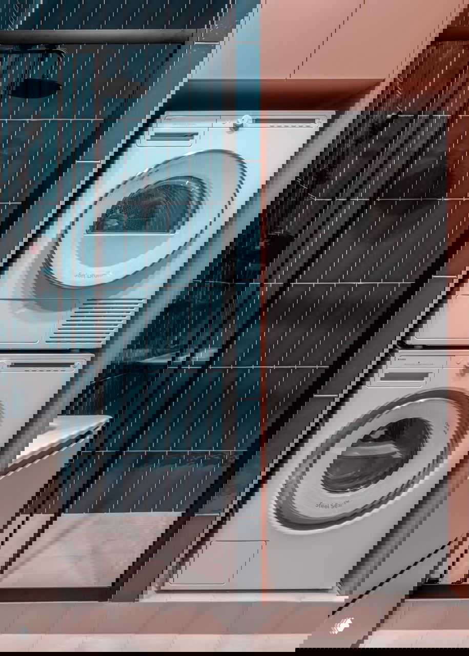 Маленькая ванная с душевой кабиной и стиральной техникой в нише, сочетание глубоких бирюзовых плиток и розовых оттенков в отделке, практичное зонирование.