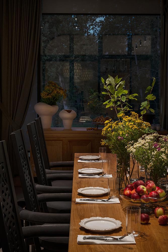 Банкетный стол вечером: деревянная столешница с фарфоровой сервировкой, вазы с полевыми цветами и миска с яблоками, создающие домашнюю атмосферу.