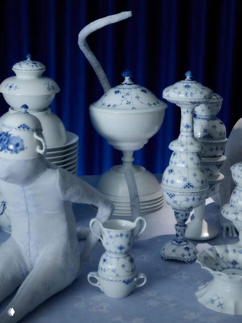 Крупный план сине-белого фарфора Royal Copenhagen: крышки, вазы и стопки блюд на столе, подчёркнуты текстурой и формой изделий.