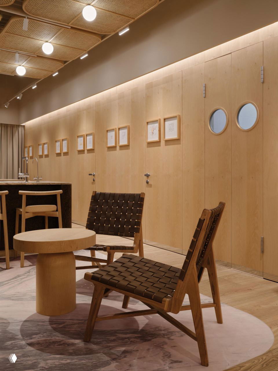 Гармоничная композиция из светлой фанерной облицовки стен, плетёных потолочных панелей, мягкой подсветки и уютной мебели в зоне кафе с розово‑мраморным покрытием на полу.
