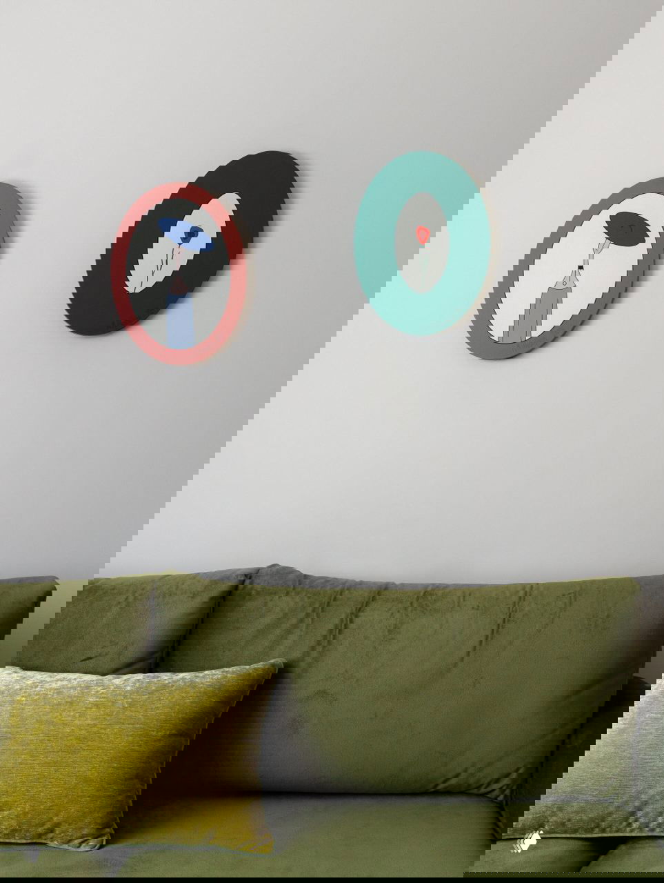 Зона гостиной с зелёным бархатным диваном и декоративными круглыми панно на светлой стене; мягкие подушки и текстильные акценты.