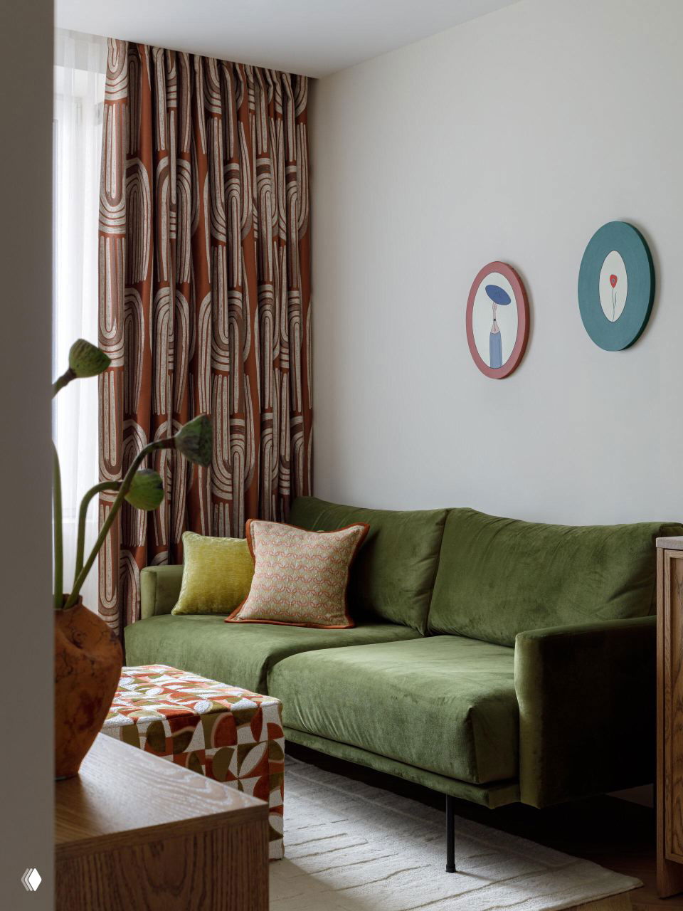 Угол гостиной с зелёным диваном, узорными шторами и мягкими декоративными подушками; атмосфера спокойного загородного интерьера.