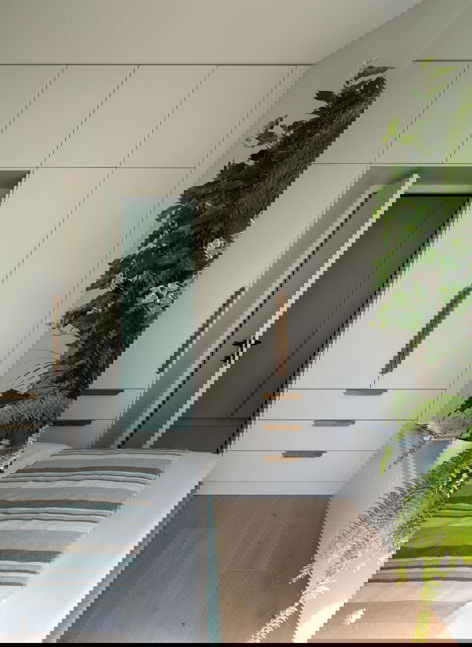 Белые встроенные шкафы и деревянные ручки в спальне, рядом стоят горшечные растения, создающие свежий и аккуратный интерьерный вид.