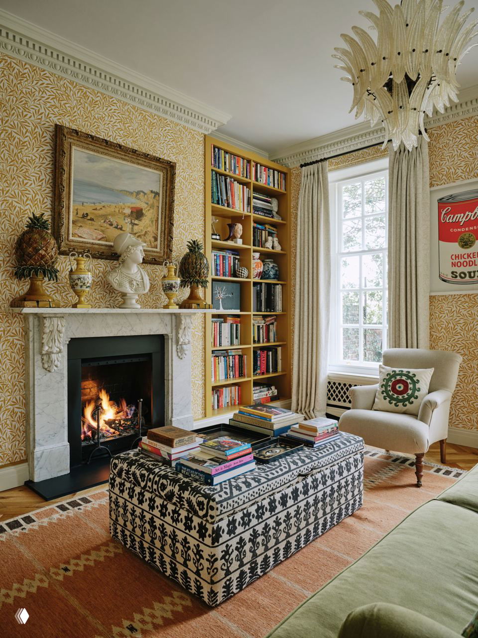 Гостиная с камином, мраморным порталом, жёлтыми растительными обоями, встроенными книжными шкафами и антикварными украшениями на каминной полке.