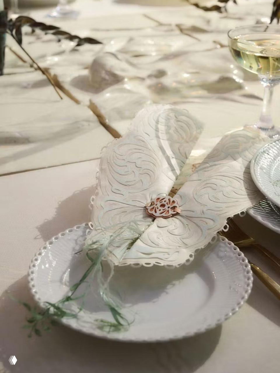 Сложенная бумажная салфетка в форме крыльев на фарфоровой тарелке — декоративный бумажный элемент сервировки с резными деталями и зелёной ниткой.
