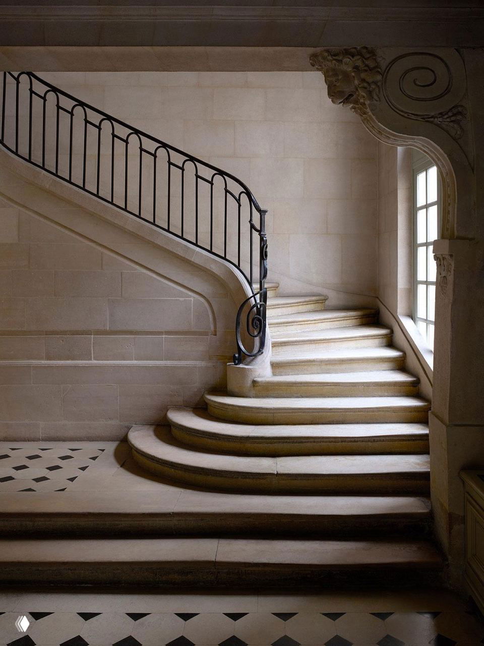 Каменная винтовая лестница в историческом подъезде дома XVII века с декоративной балюстрадой и световым окном, подчёркивающим архитектуру.